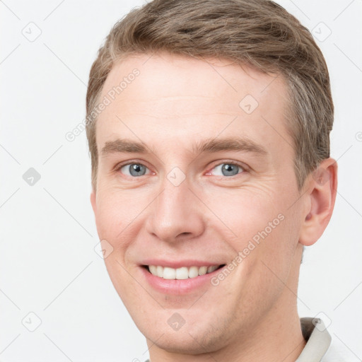 Joyful white young-adult male with short  brown hair and grey eyes