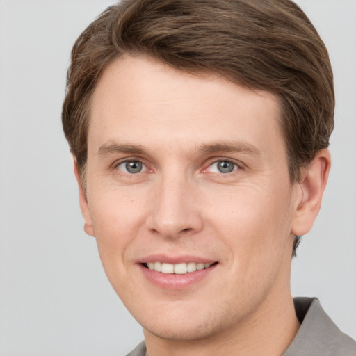 Joyful white young-adult male with short  brown hair and grey eyes