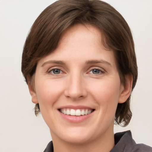 Joyful white young-adult female with medium  brown hair and grey eyes