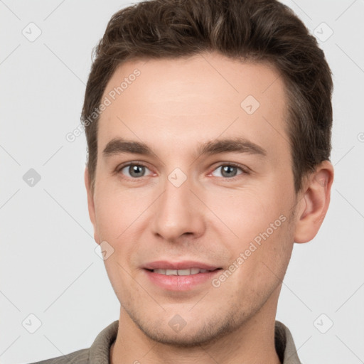 Joyful white young-adult male with short  brown hair and grey eyes