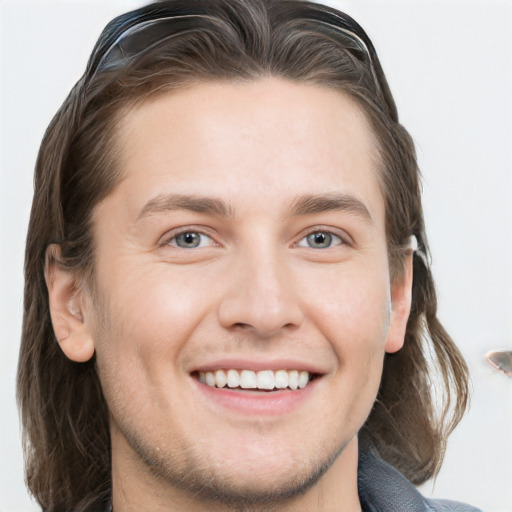 Joyful white young-adult male with long  brown hair and brown eyes