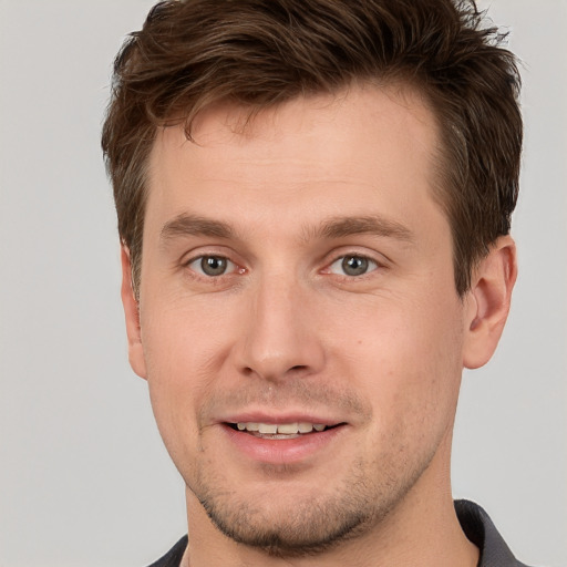 Joyful white young-adult male with short  brown hair and grey eyes