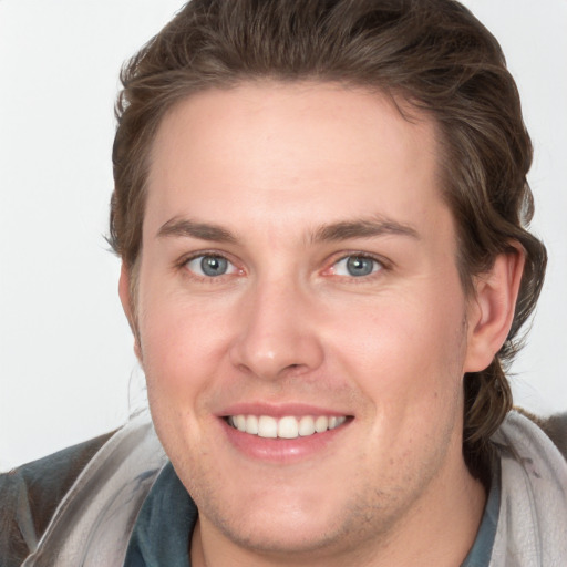 Joyful white young-adult male with long  brown hair and grey eyes