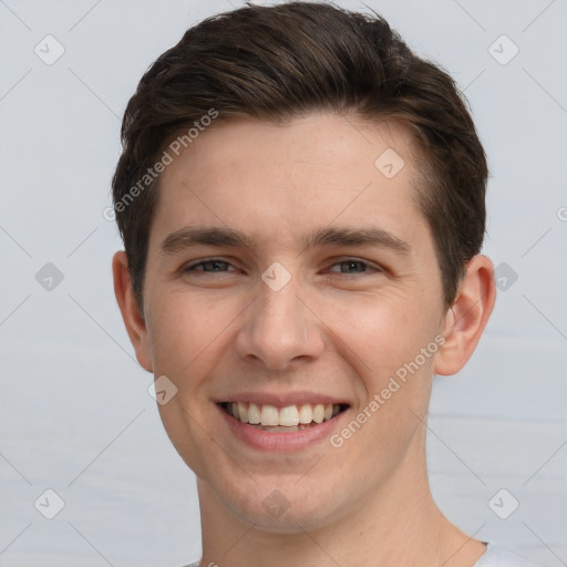 Joyful white young-adult male with short  brown hair and grey eyes