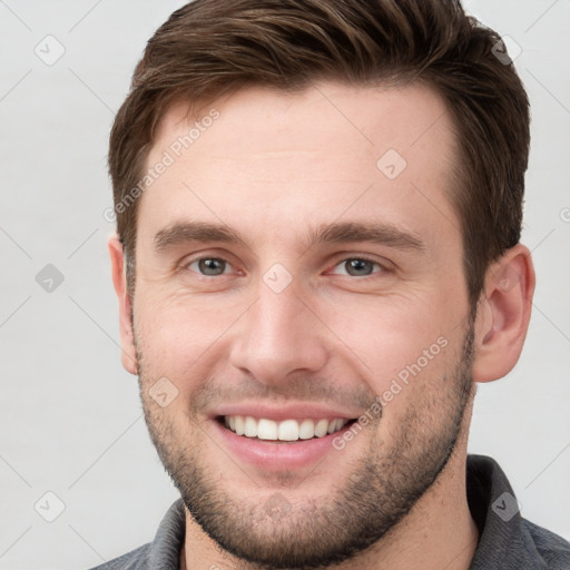 Joyful white young-adult male with short  brown hair and grey eyes