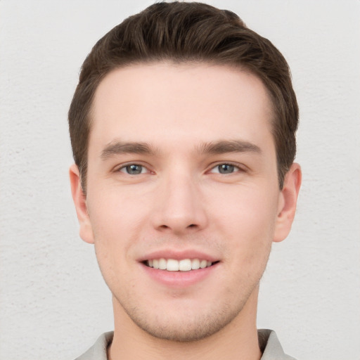 Joyful white young-adult male with short  brown hair and grey eyes