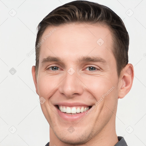 Joyful white young-adult male with short  brown hair and grey eyes