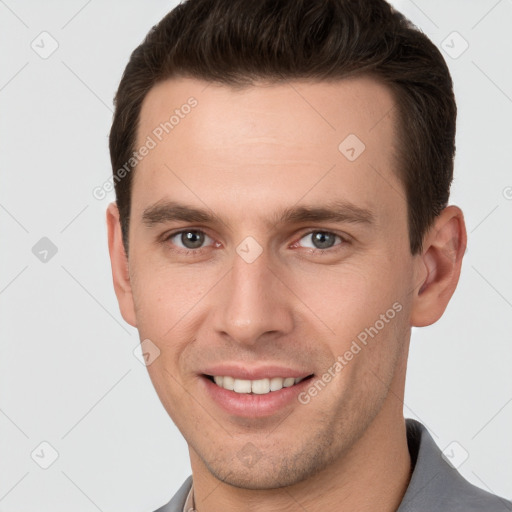 Joyful white young-adult male with short  brown hair and grey eyes