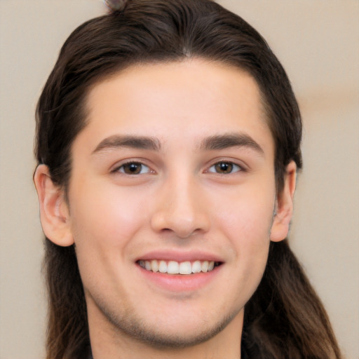Joyful white young-adult male with long  brown hair and brown eyes