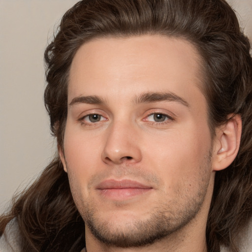 Joyful white young-adult male with long  brown hair and brown eyes