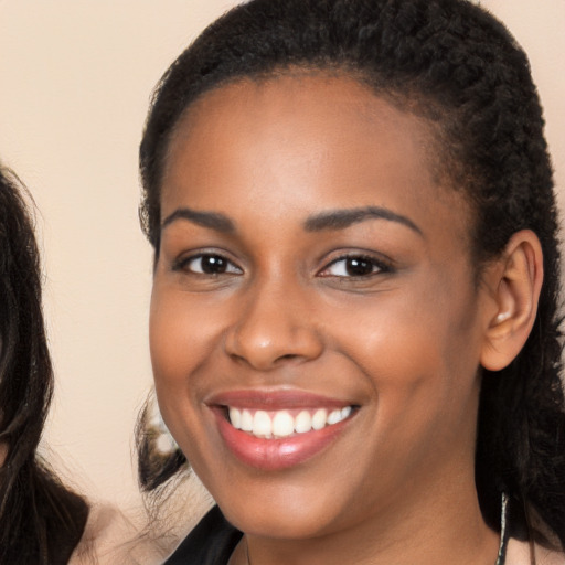 Joyful black young-adult female with long  brown hair and brown eyes