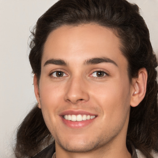 Joyful white young-adult male with long  brown hair and brown eyes