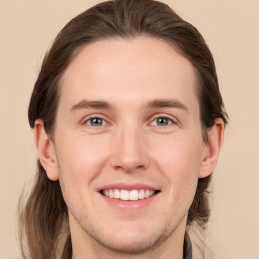 Joyful white young-adult male with long  brown hair and grey eyes