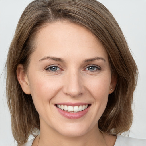 Joyful white young-adult female with medium  brown hair and grey eyes