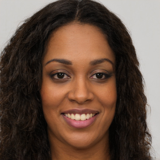Joyful black young-adult female with long  brown hair and brown eyes