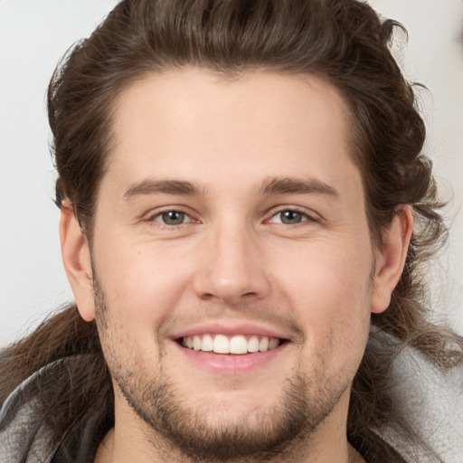 Joyful white young-adult male with long  brown hair and brown eyes