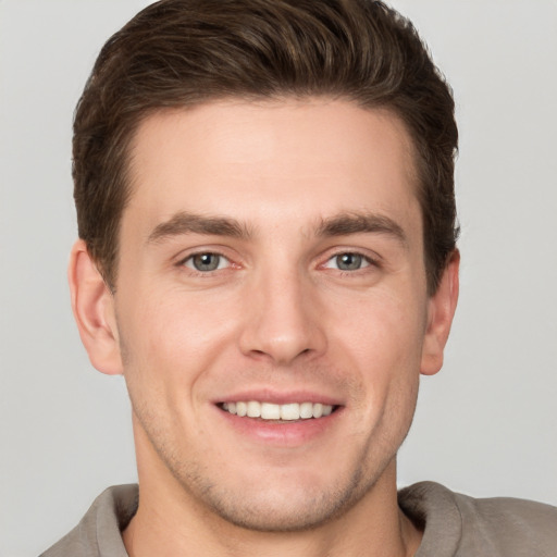 Joyful white young-adult male with short  brown hair and grey eyes