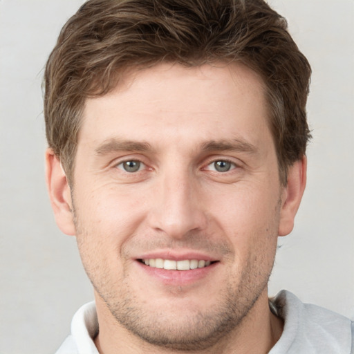 Joyful white young-adult male with short  brown hair and grey eyes