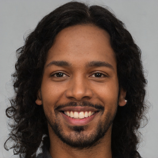 Joyful black young-adult male with long  black hair and brown eyes