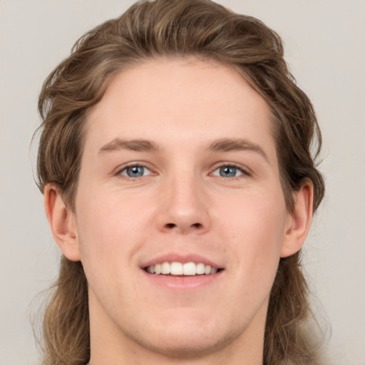 Joyful white young-adult male with long  brown hair and grey eyes