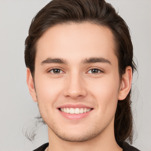 Joyful white young-adult male with long  brown hair and brown eyes