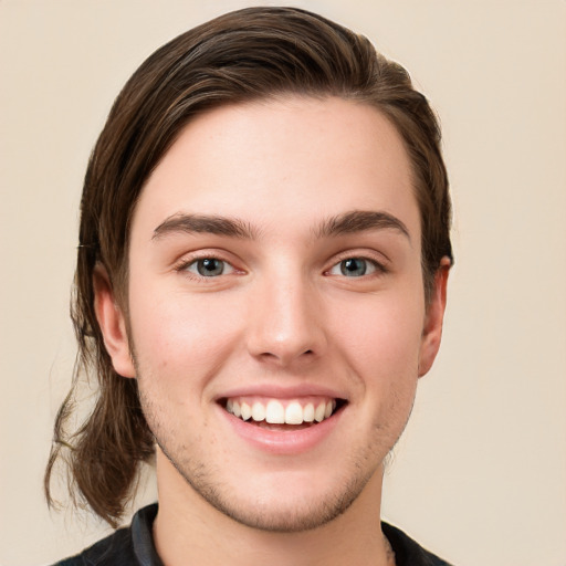 Joyful white young-adult male with long  brown hair and grey eyes