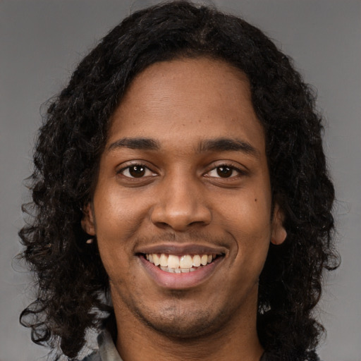 Joyful black young-adult male with long  black hair and brown eyes