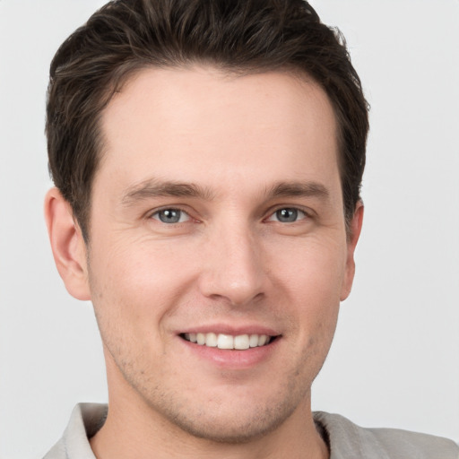 Joyful white young-adult male with short  brown hair and grey eyes