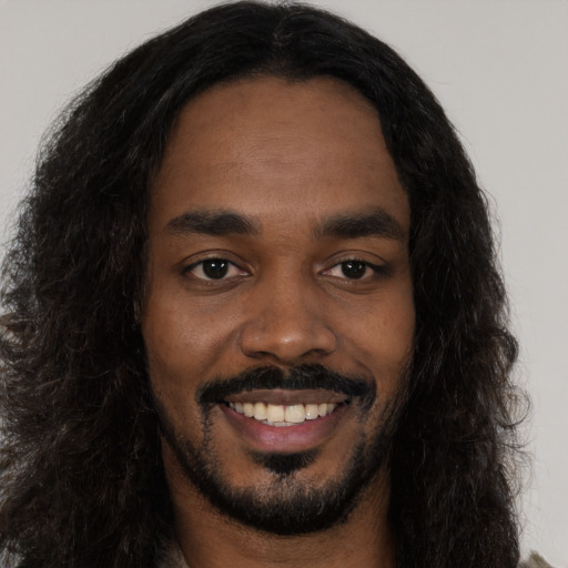 Joyful black young-adult male with long  black hair and brown eyes